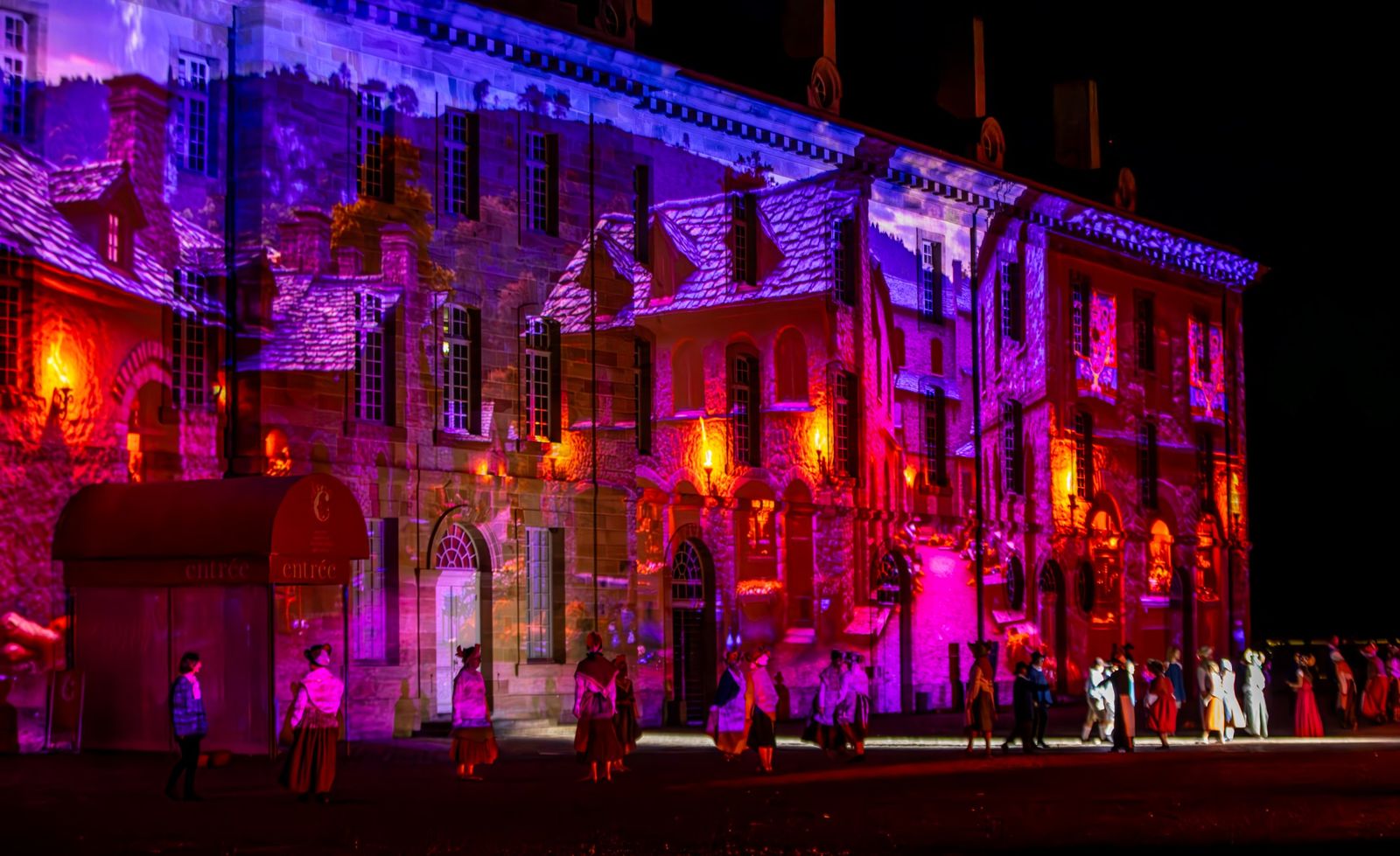 Une façade rouge et violette éclairée, devant les figurants
