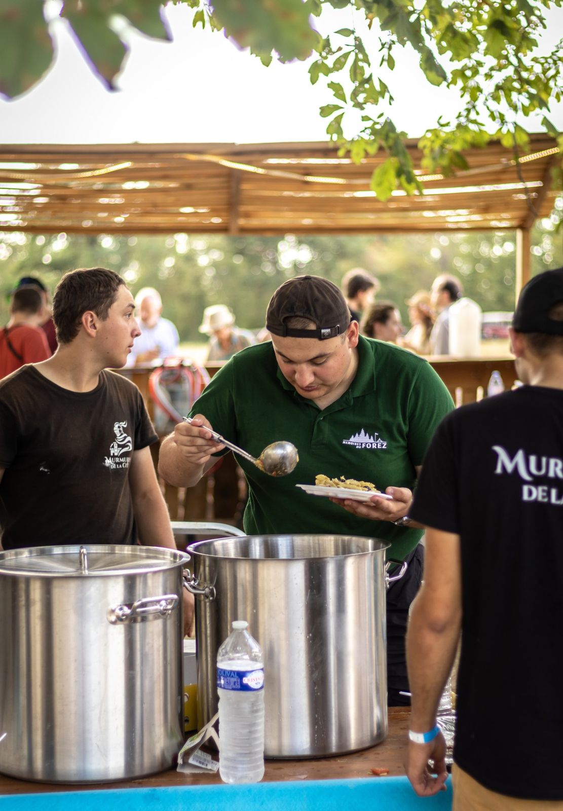 Des bénévoles servent le repas des équipes devant de grandes marmites