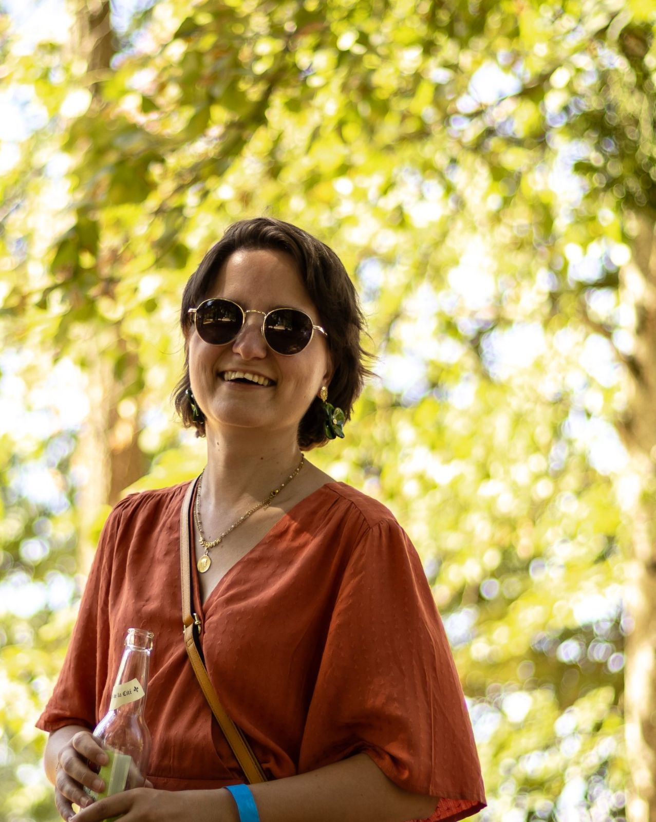 Une spectatrice souriante, une bouteille à la main, sous les arbres